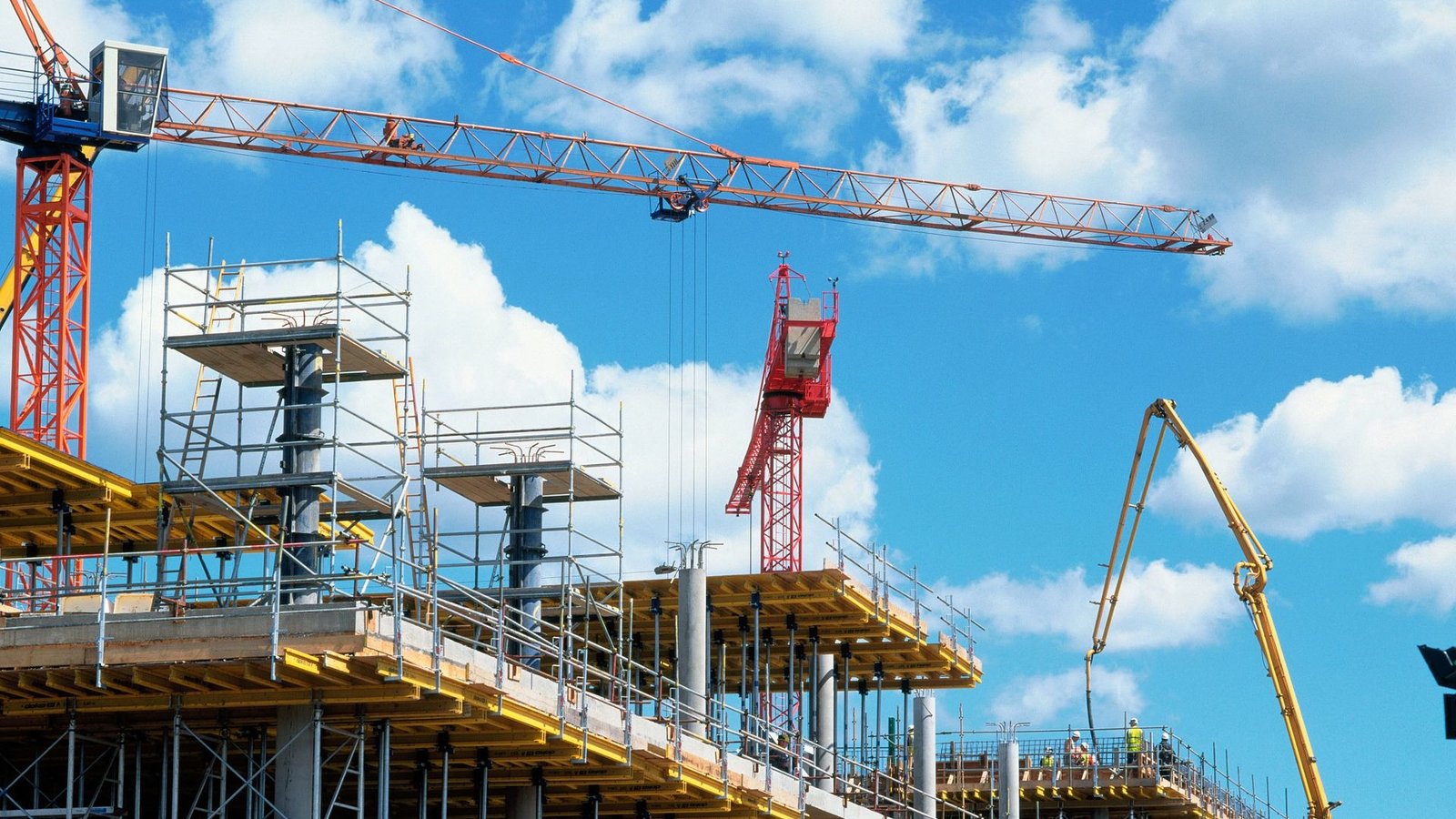 Baustelle eines mehrgeschossigen Wohngebäudes mit Turmdrehkran, Gerüst und Bauarbeitern, die eine Betondecke vorbereiten